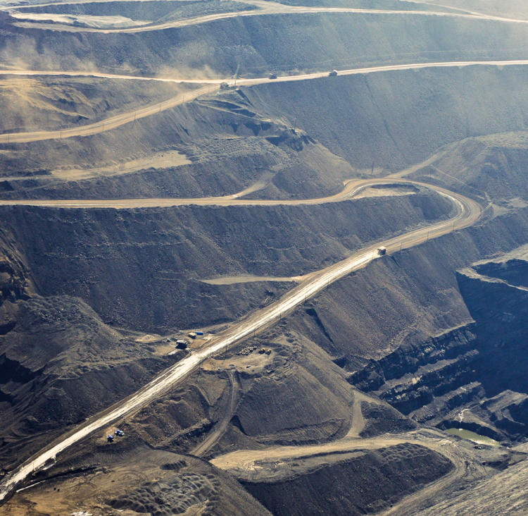 Image of an open pit coal mines with massive trucks driving down roads, coal dust in the air